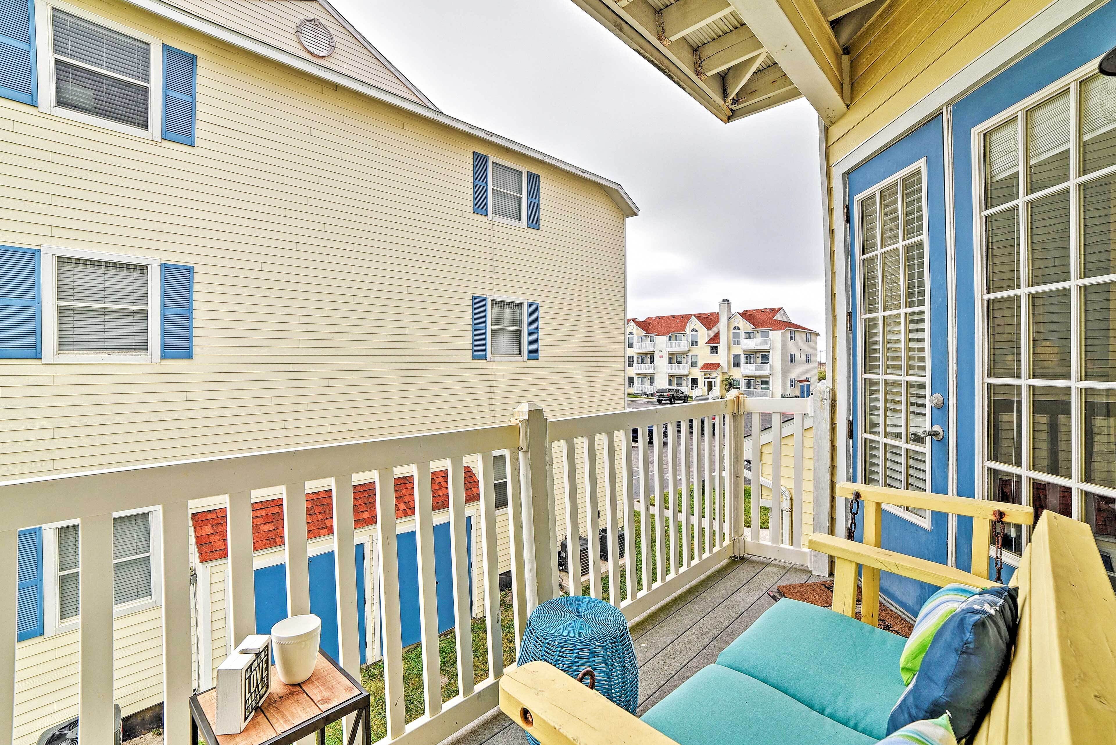 A balcony with a wooden bench and a table, overlooking a row of houses with blue shutters.