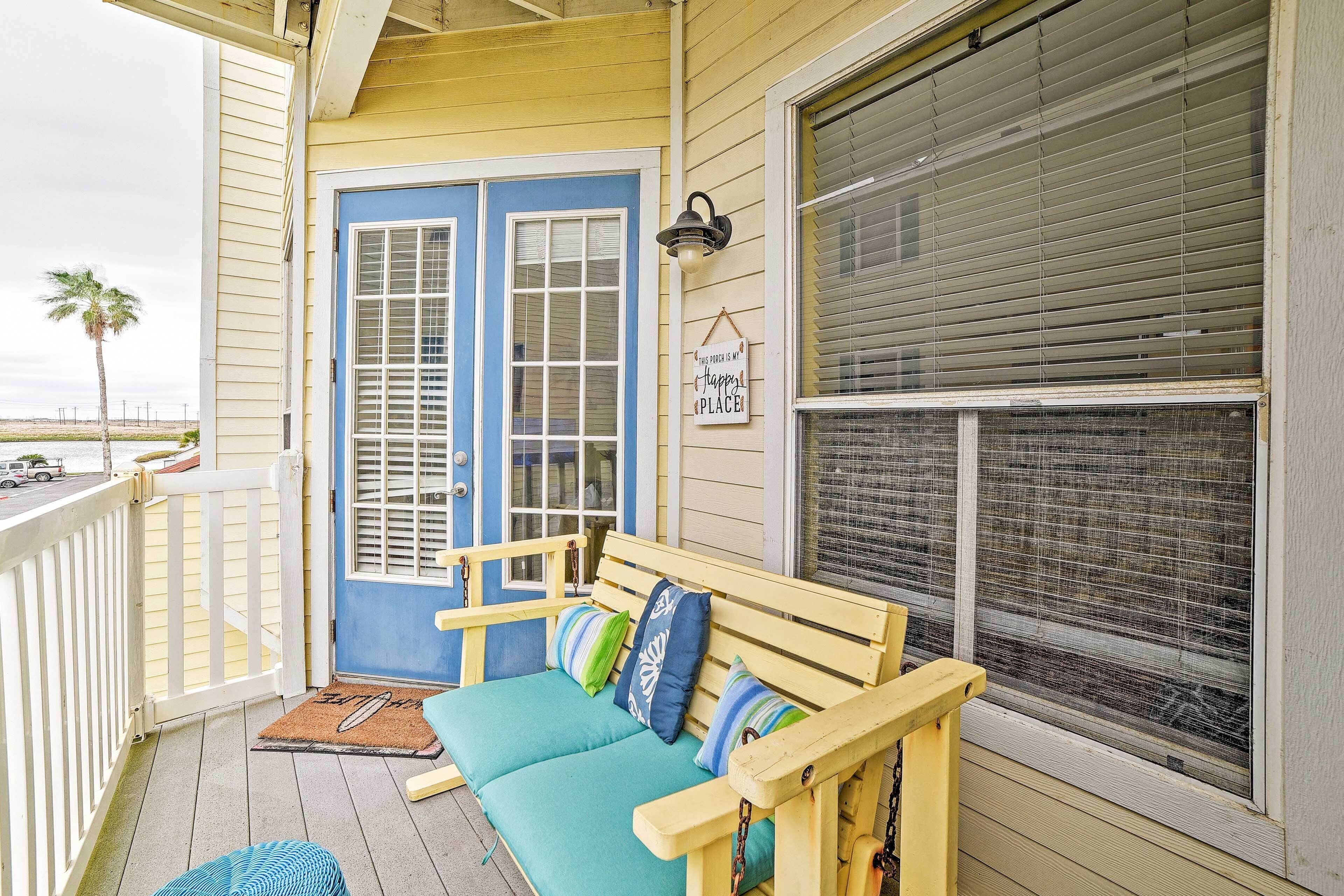 A porch with a blue door, a bench with cushions, and a sign that says "happy place."