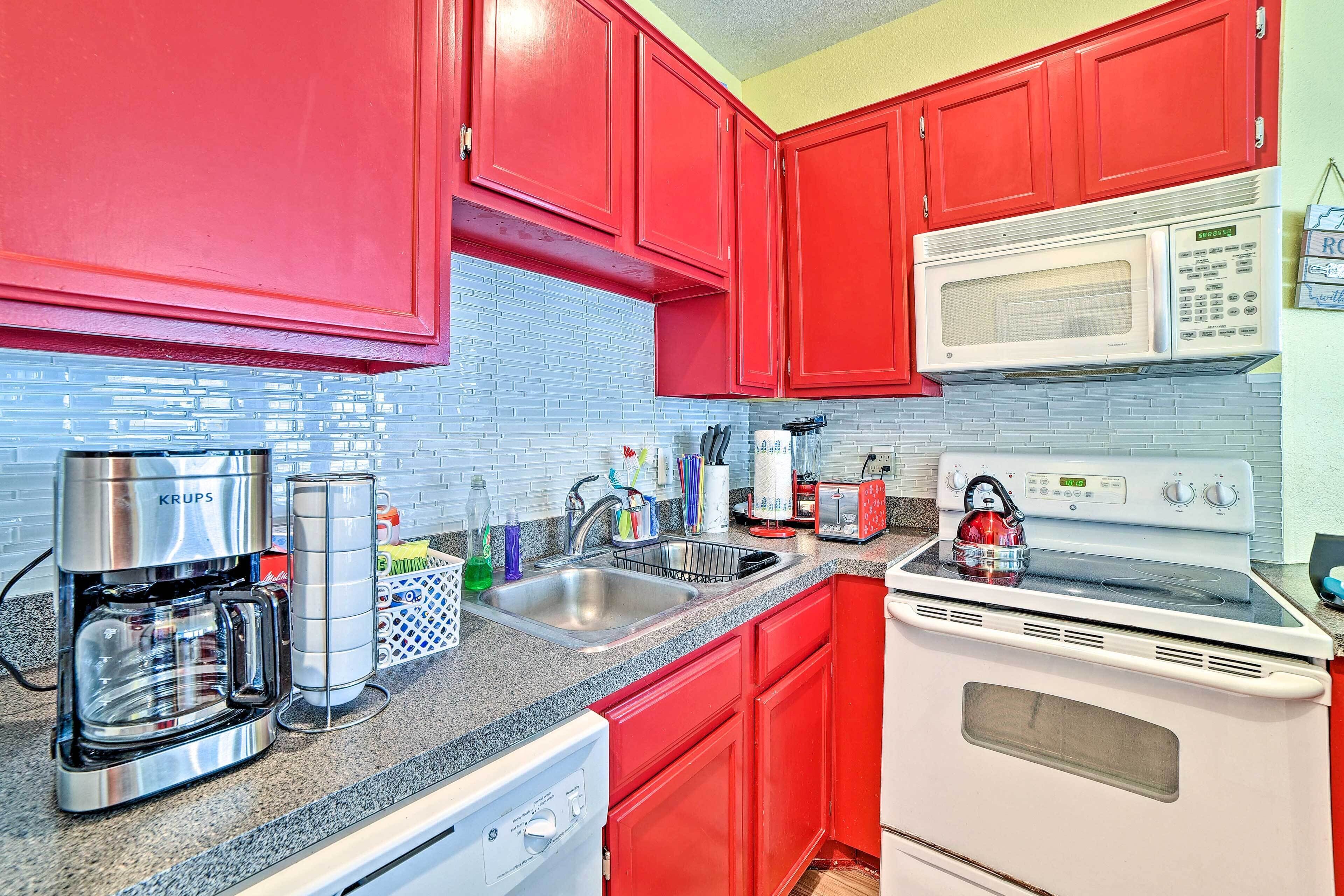 A kitchen with red cabinets, a white microwave, a stove, and a coffee maker.