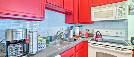 A kitchen with red cabinets, a white microwave, a stove, and a coffee maker.