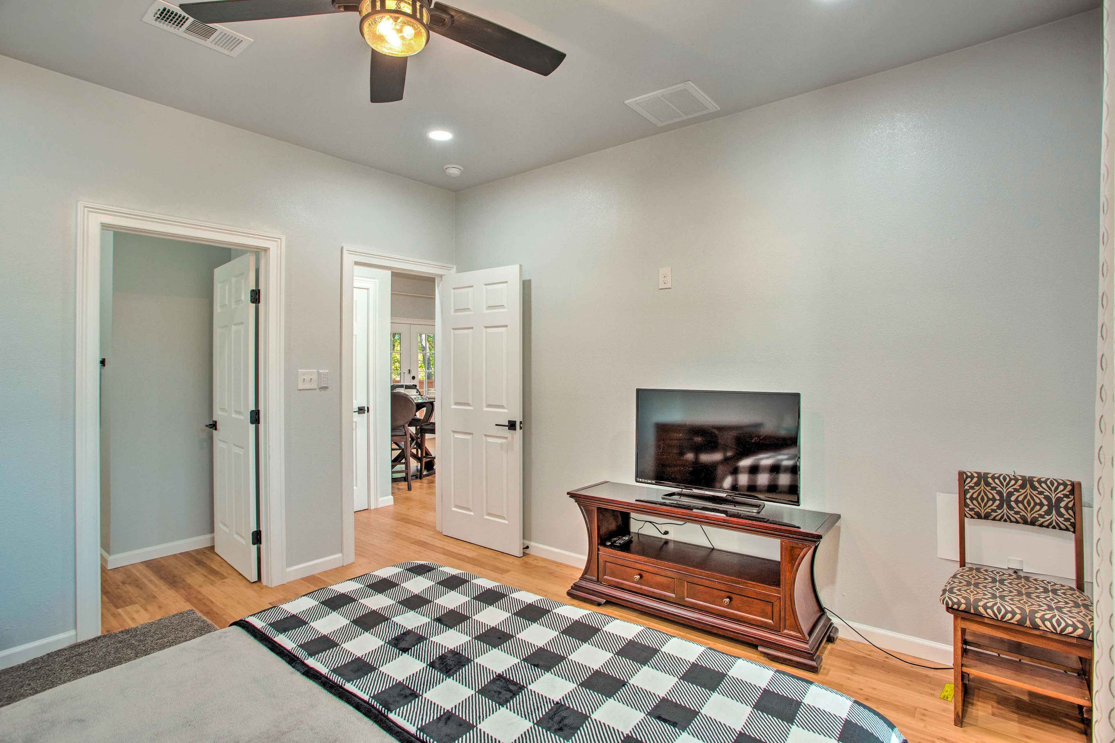 A room with a ceiling fan, a television on a wooden stand, a patterned rug, and a chair.