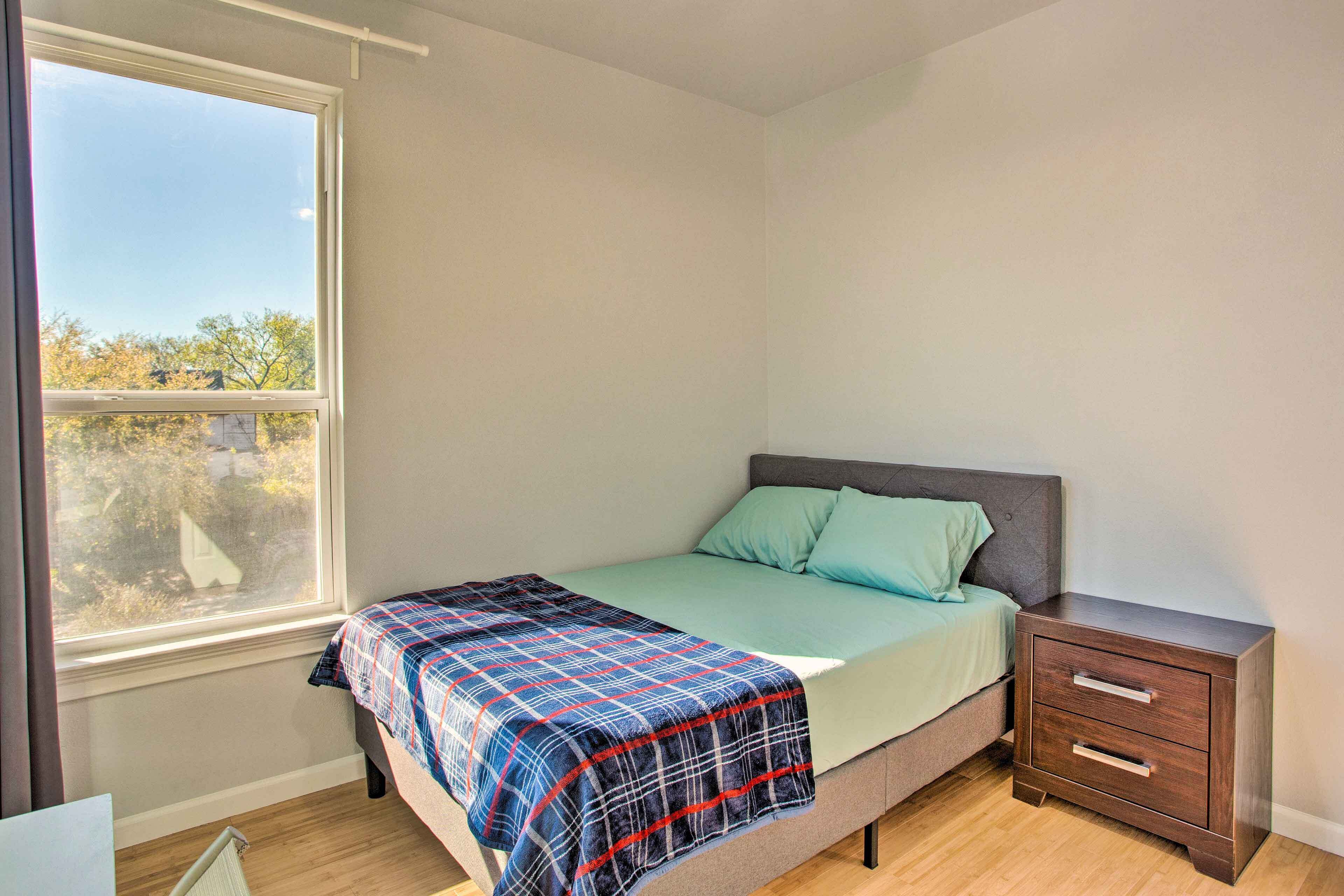 A bedroom with a bed, a nightstand, a window, and a view of trees outside.