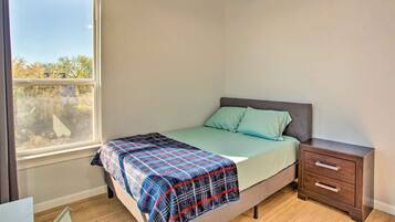 A bedroom with a bed, a nightstand, a window, and a view of trees outside.