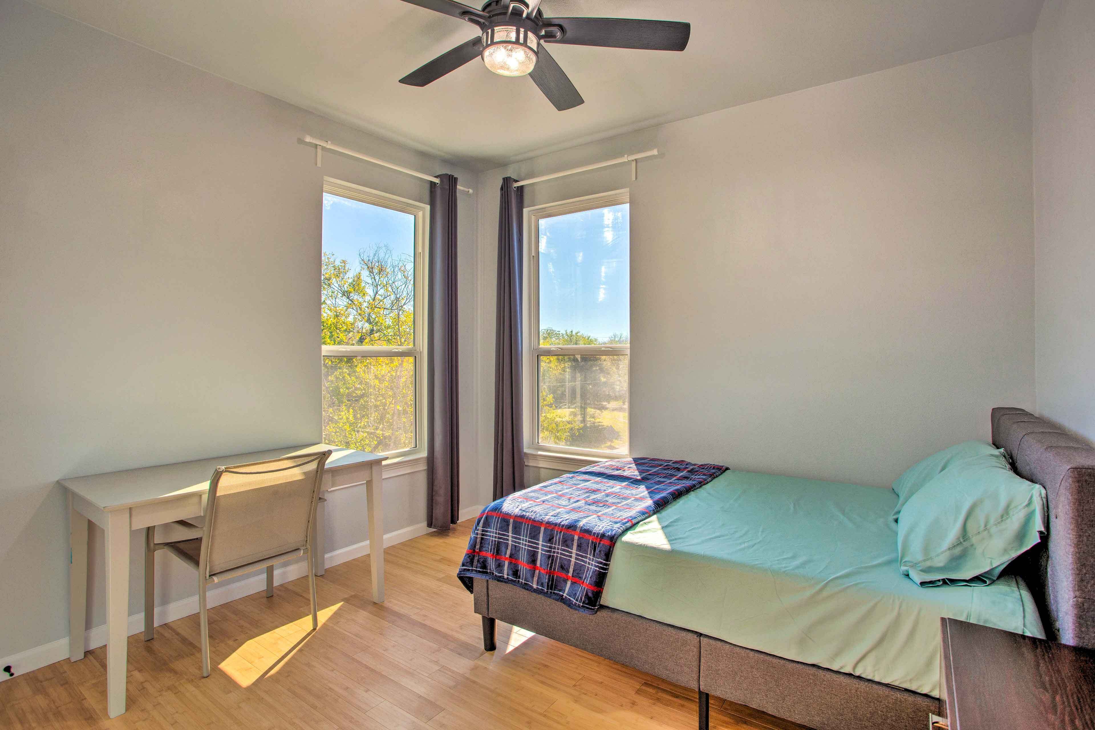 A bedroom with a bed, a desk, and a ceiling fan.