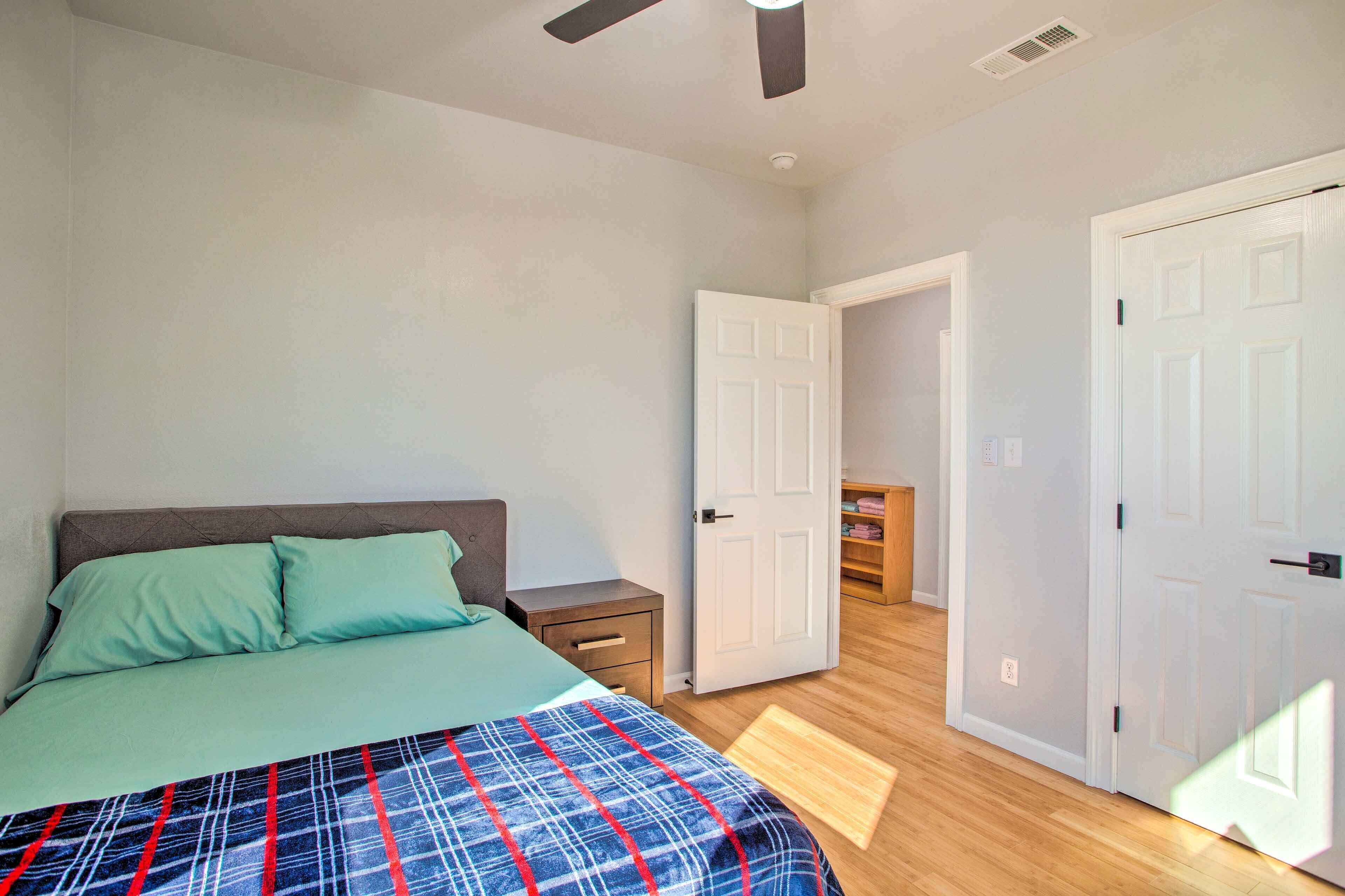 Quarto com cama, mesa de cabeceira e porta que dá para outro cômodo.