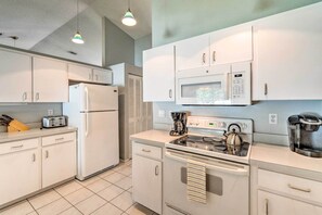 A modern kitchen with white cabinets, a refrigerator, a microwave, a stove, and a coffee maker.