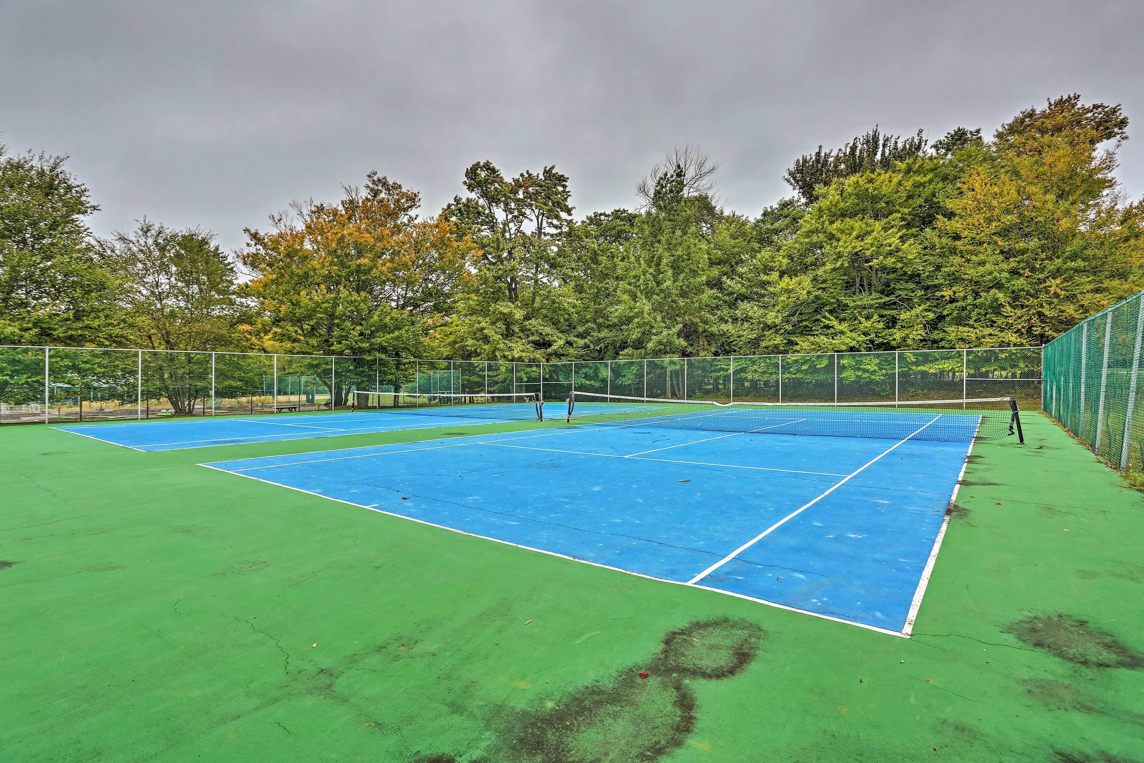 A tennis court with a net, surrounded by a fence and trees.