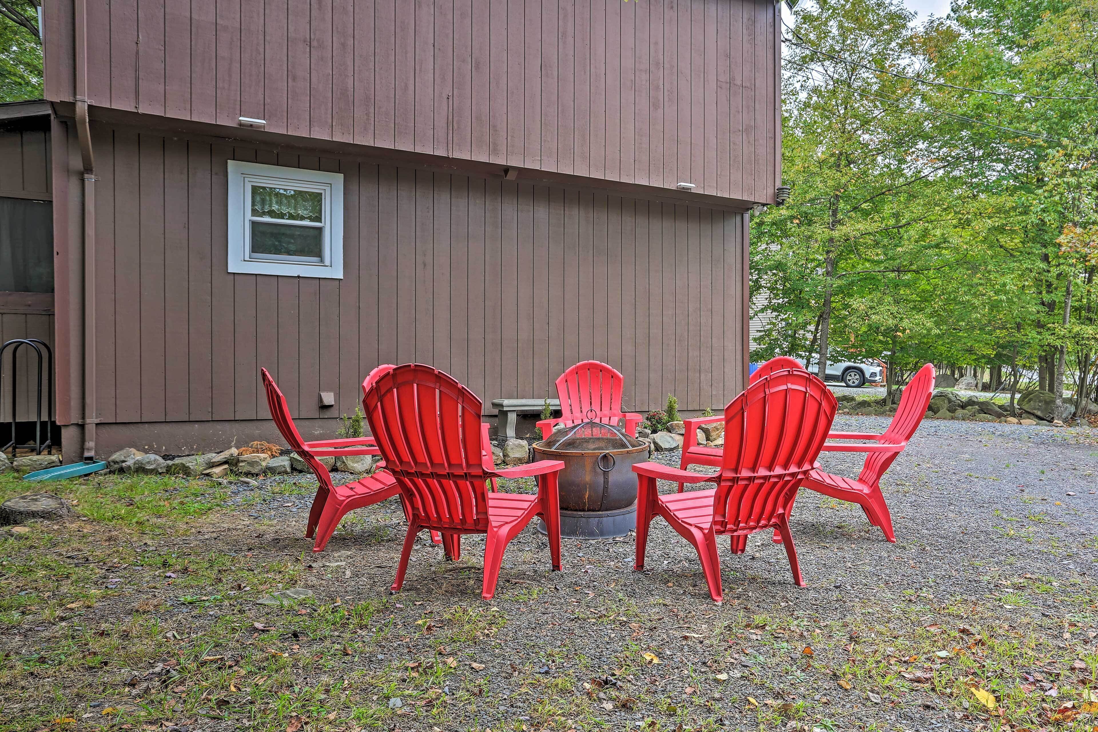 Une terrasse avec quatre chaises Adirondack rouges disposées autour d’un foyer en métal.