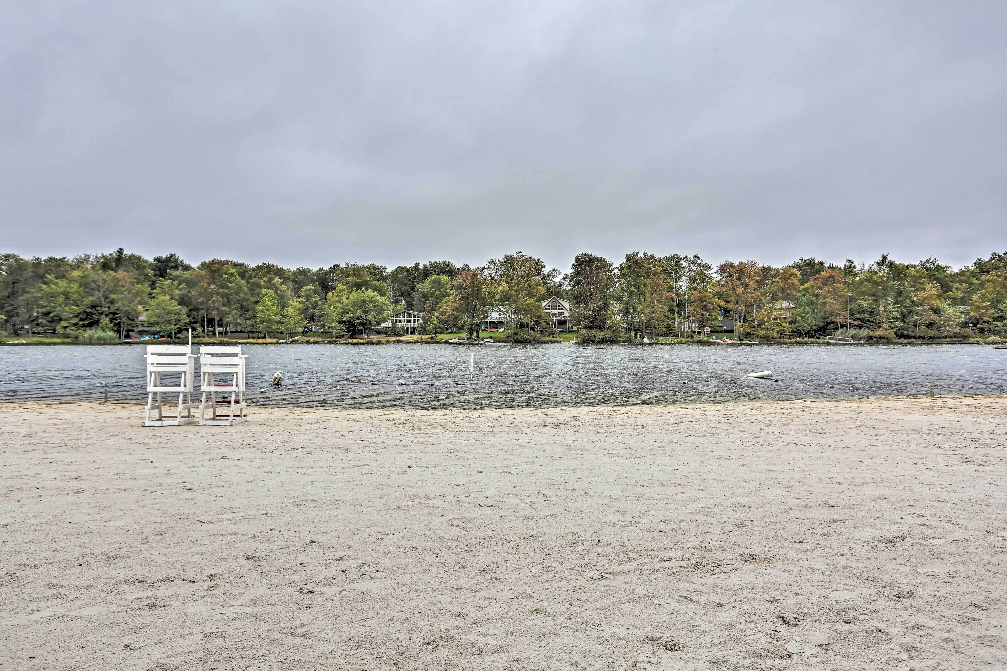 A beach with two white chairs and a lake with houses in the background.