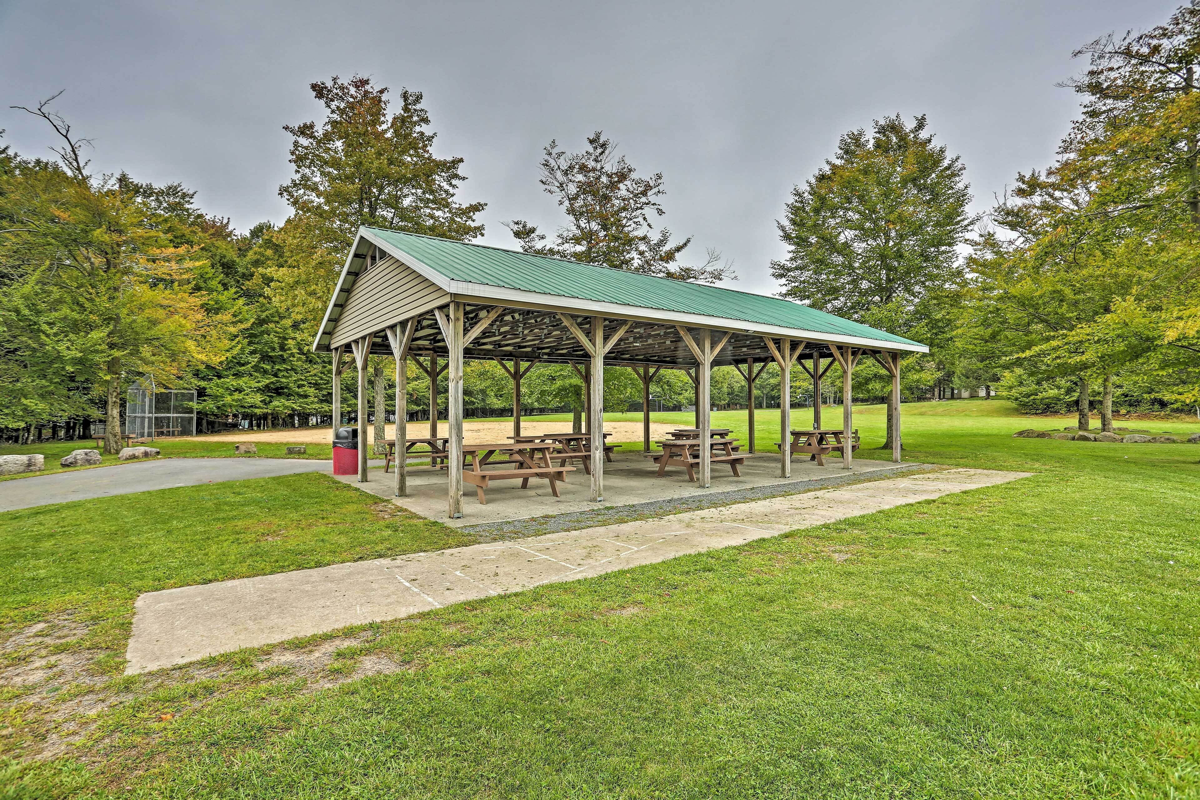 A covered picnic area with benches and picnic tables, surrounded by grass and trees.