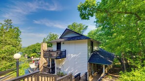 A white building with a dark roof, a balcony, and a wooden staircase leading to a covered area. - Dock, Boat Slip & View: Lakefront Tan-tar-a Home! (Osage Beach)