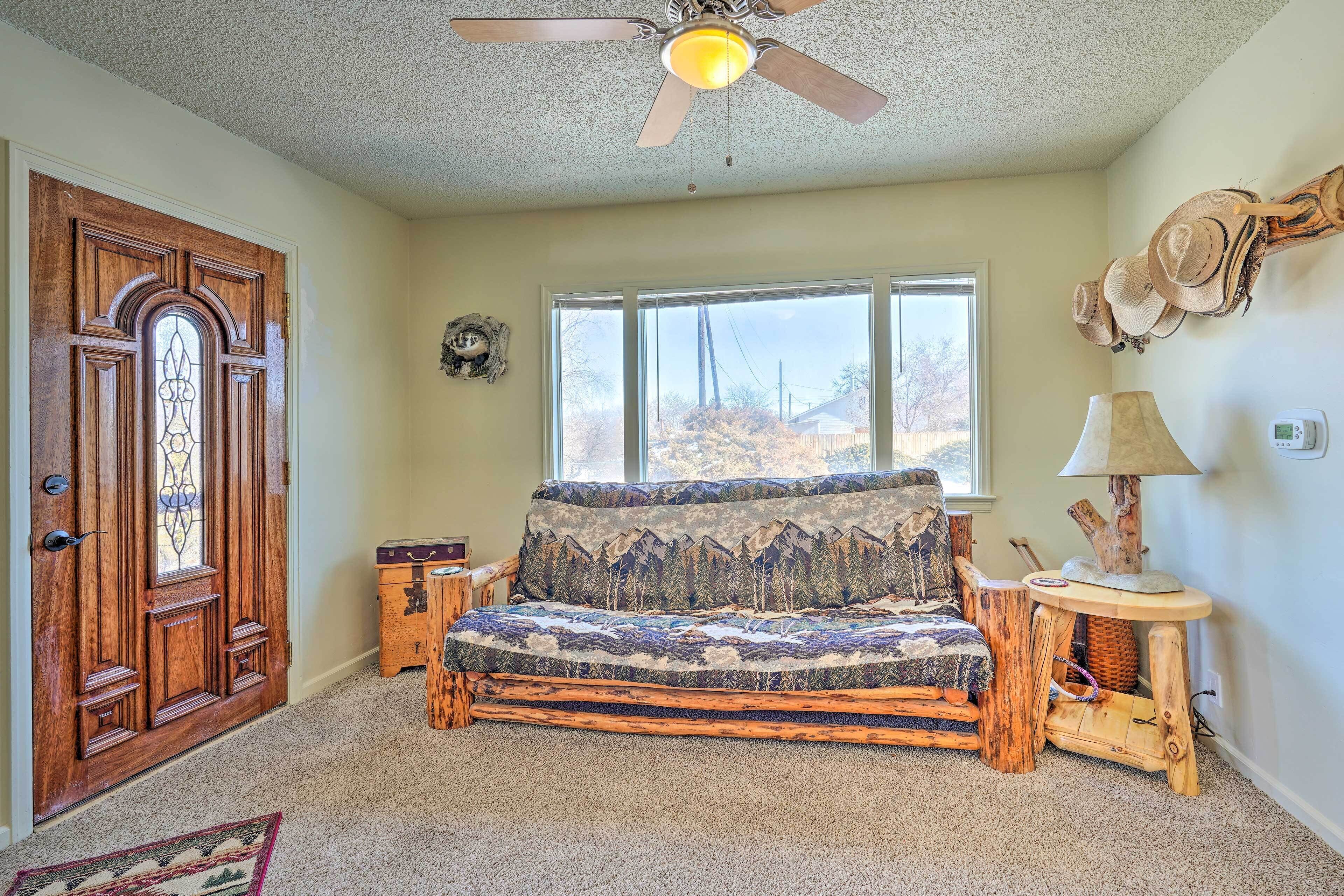 A cozy room with a wooden door, a window with a view, a ceiling fan, and a unique sofa made from wood.
