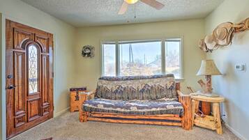 A cozy room with a wooden door, a window with a view, a ceiling fan, and a unique sofa made from wood.