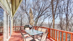 Eine überdachte Terrasse mit einem Glastisch und Stühlen, umgeben von einem roten Geländer, mit Blick auf ein bewaldetes Gebiet.