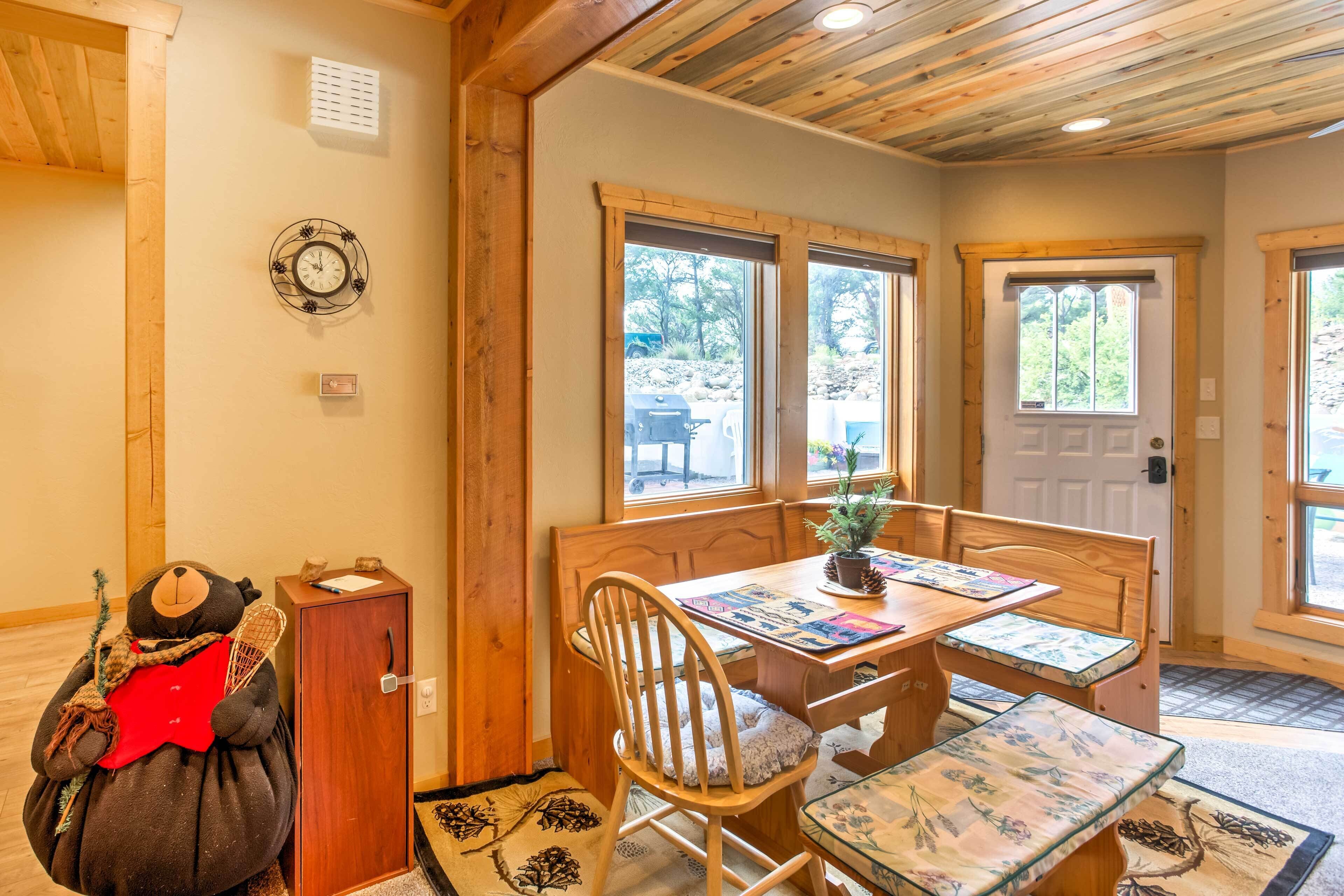 Una habitación acogedora con techo de madera, un banco de madera, una mesa con planta en maceta y una puerta con ventanas.