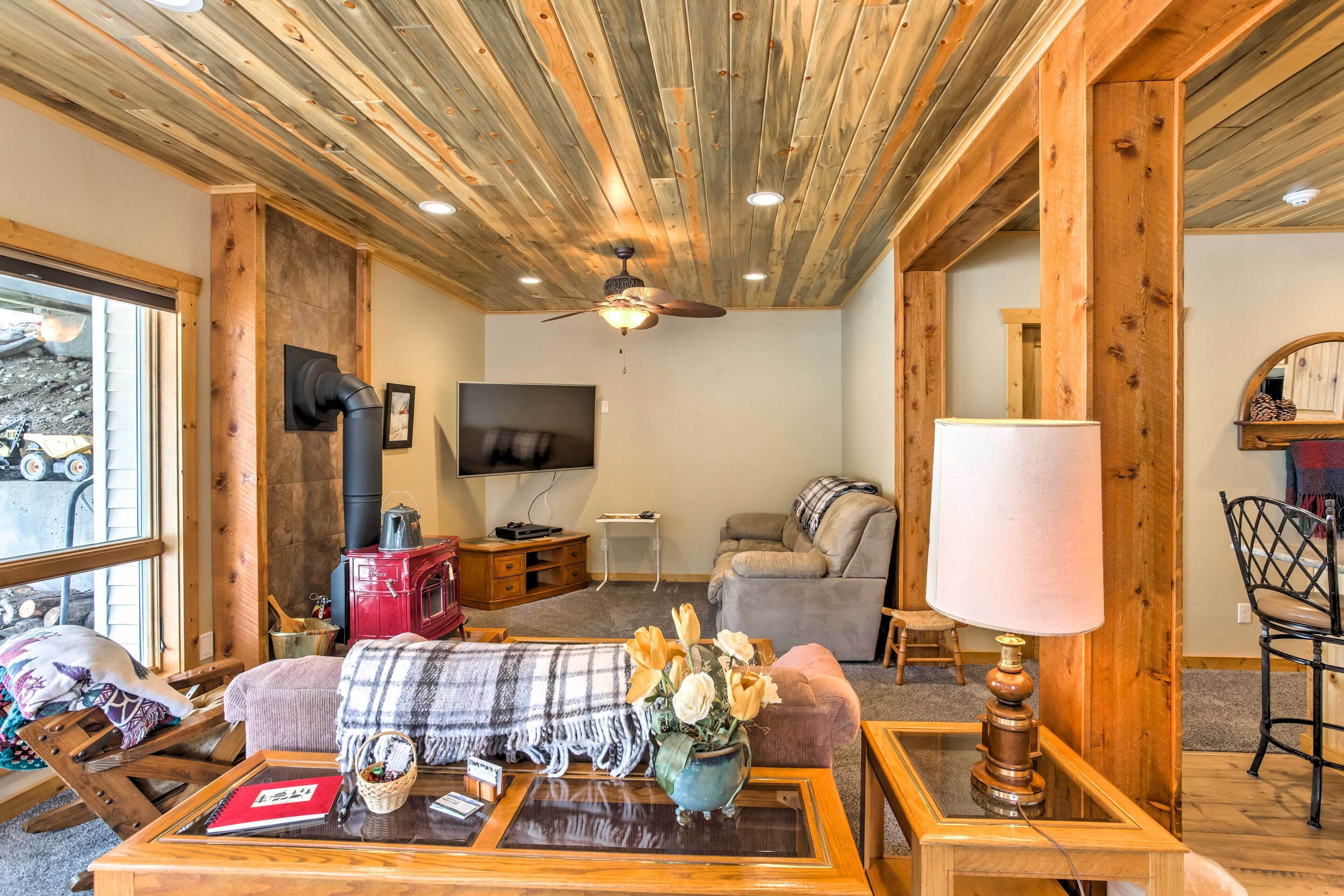 A cozy living room with a wooden ceiling, a fireplace, a television, and comfortable seating.