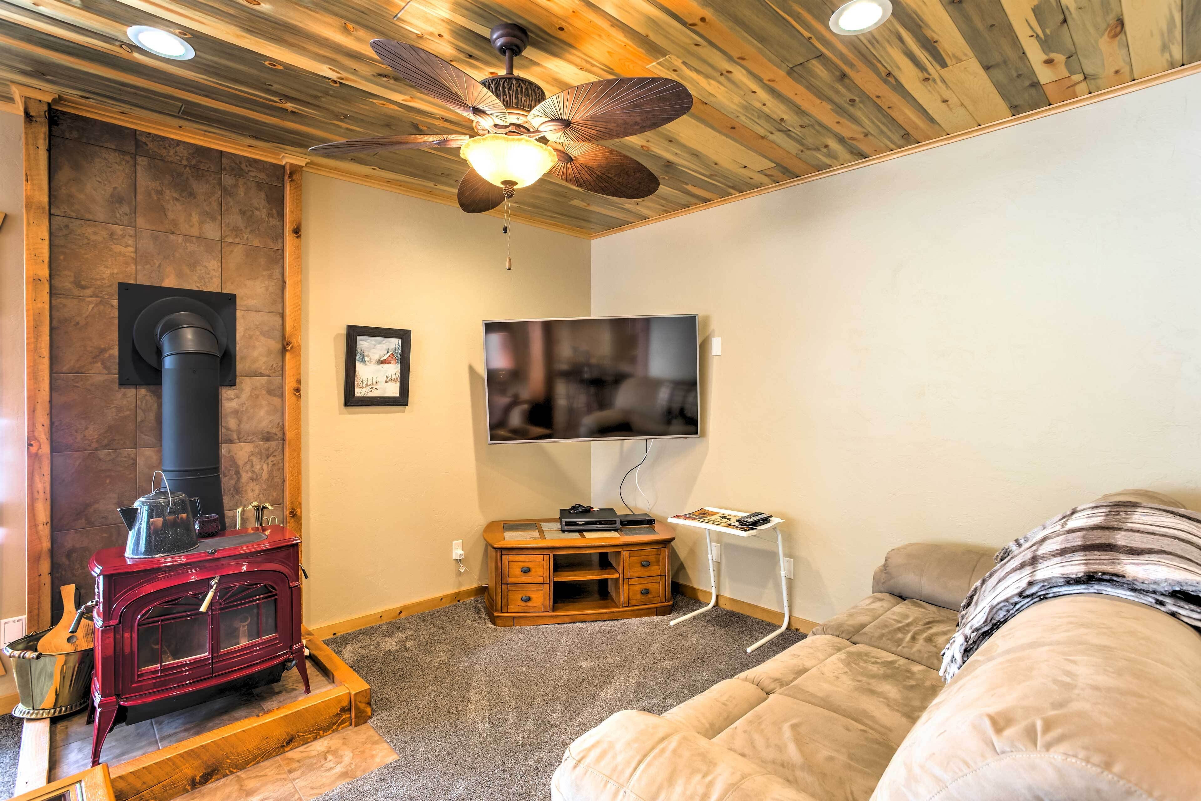 A cozy room with a wood-burning stove, a ceiling fan, a television, and a comfortable couch.