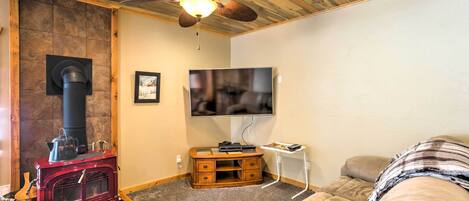 Una habitación acogedora con estufa de leña, ventilador de techo, televisión y un sofá cómodo.