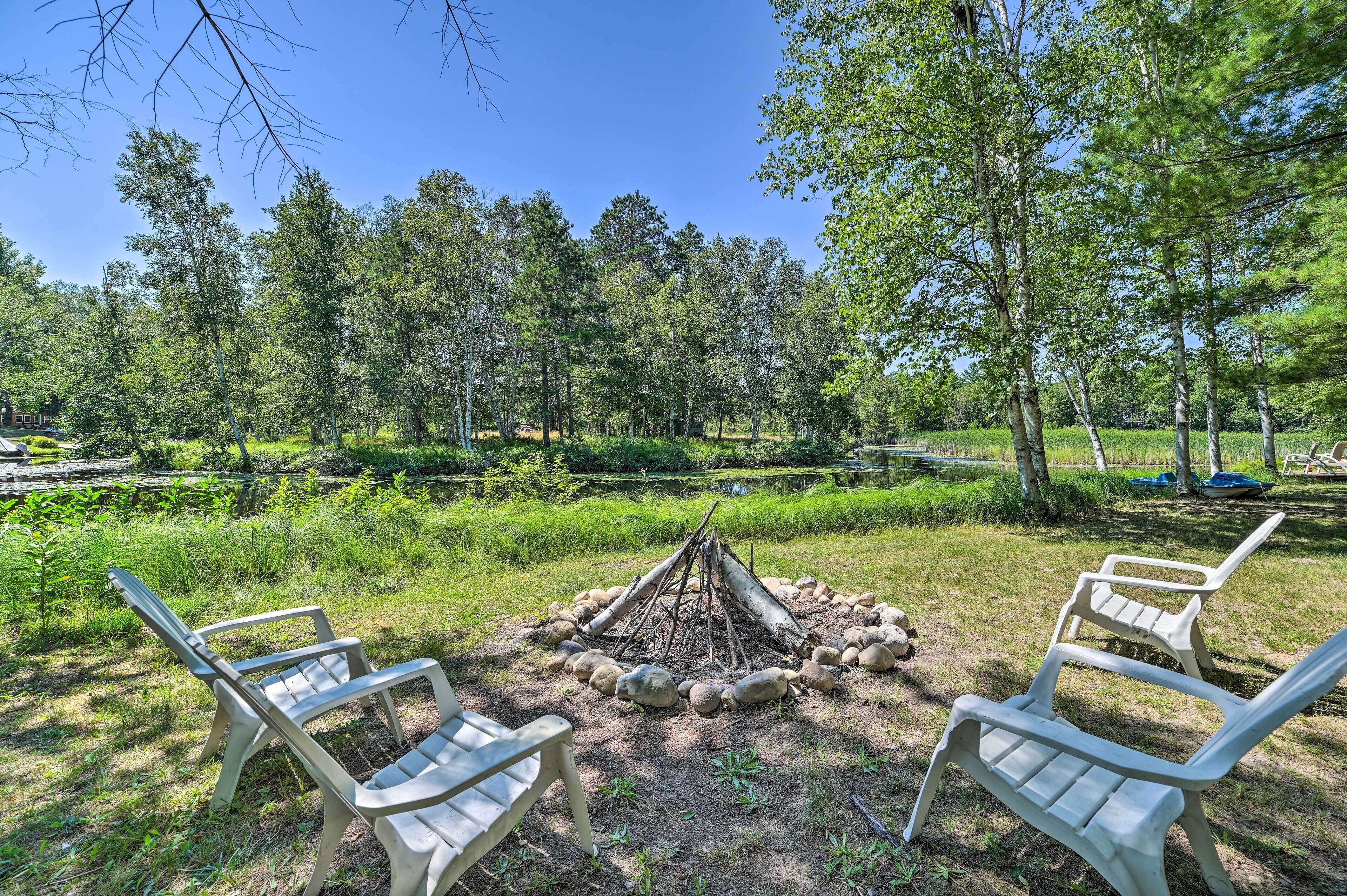 A campsite with a fire pit surrounded by rocks and three plastic chairs.