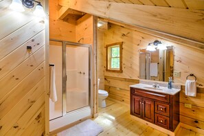 Experience a modern bathroom with a glass-enclosed shower, white toilet, and wooden vanity.
