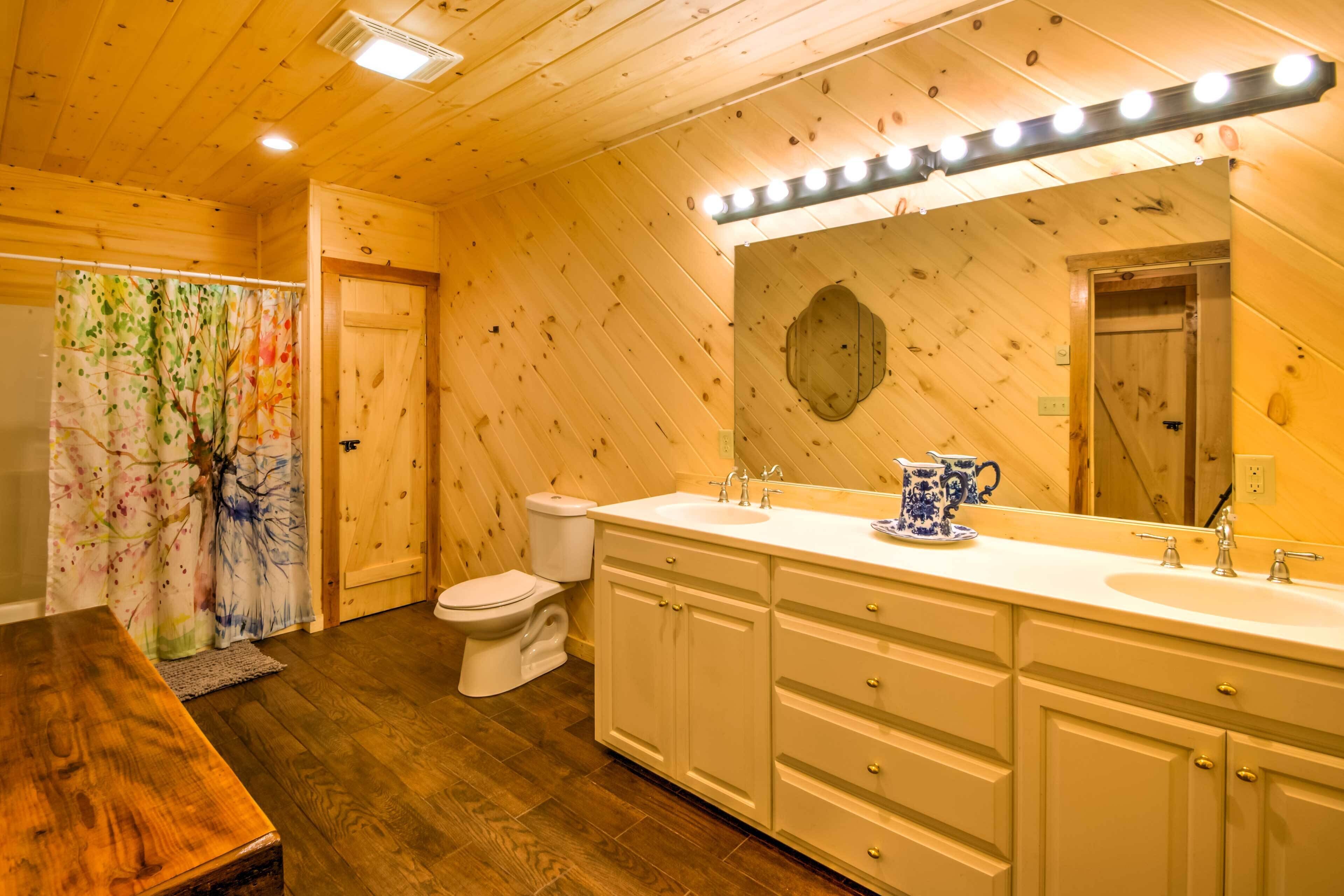 Un baño de cabaña de madera con piso de madera, un inodoro blanco, un lavamanos con espejo y un mueble de tocador con cajones.