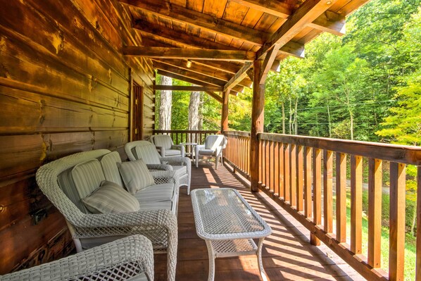Relax on the covered porch with a sofa and chairs, surrounded by a forest view.