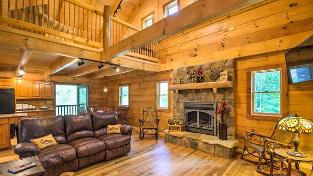 Ein Holzblockhaus-Interieur mit Ledersofa, Kamin aus Stein und Essbereich.
