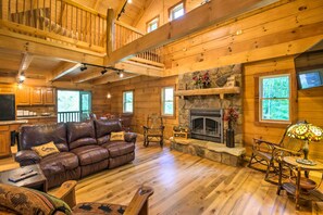 Cozy cabin-style room with a leather sofa, stone fireplace, and dining area.