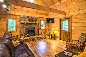 Cozy cabin interior with a stone fireplace, leather sofa, and wooden dining table.
