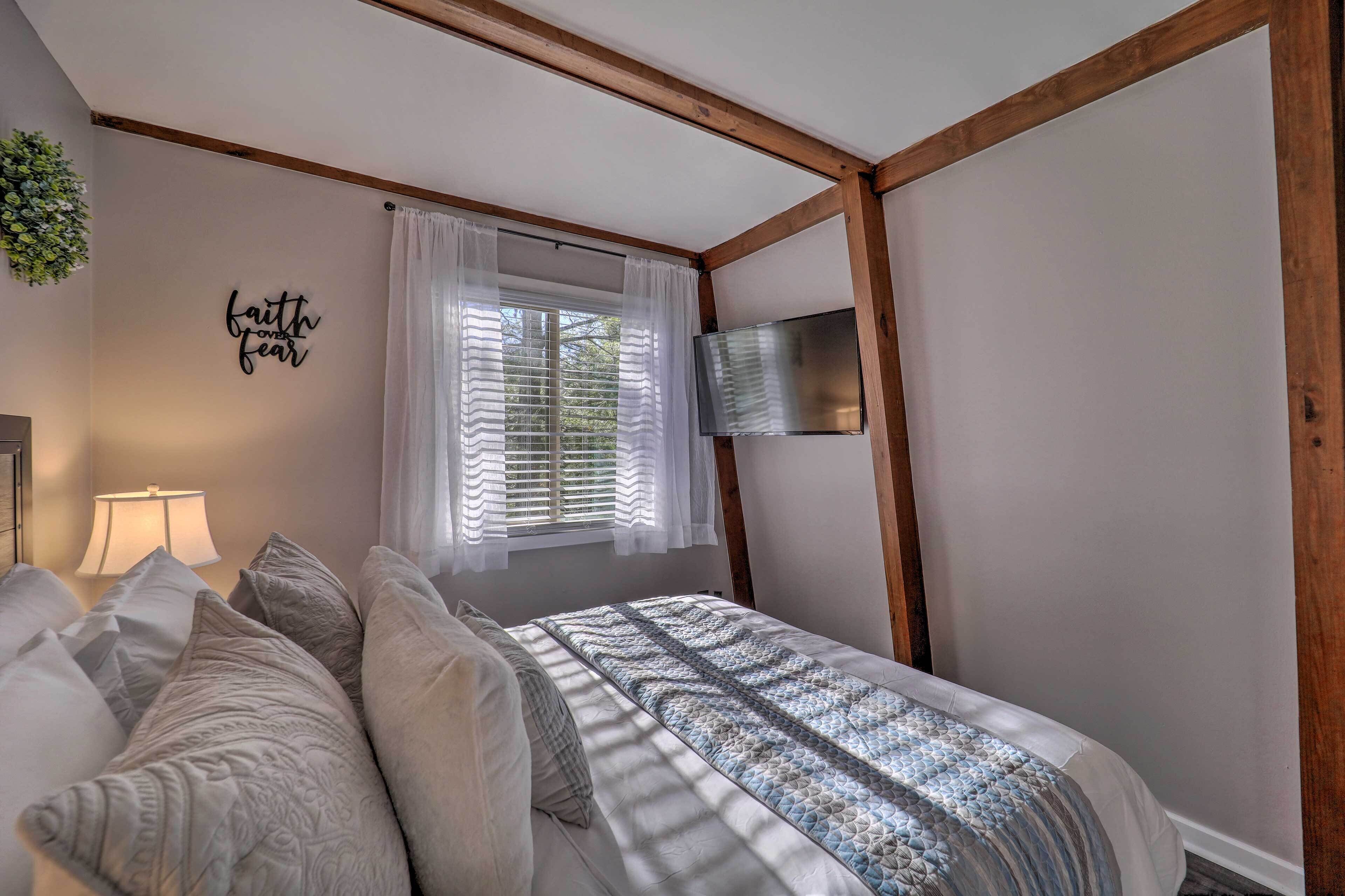 A bedroom with a bed, a TV mounted on the wall, a window with curtains, and a wall decoration.