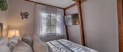 A bedroom with a bed, a TV mounted on the wall, a window with curtains, and a wall decoration.