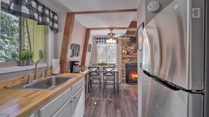Une cuisine moderne dotée d’un réfrigérateur en acier inoxydable, de plans de travail en bois, d’une cheminée en pierre et d’un coin repas avec des chaises.