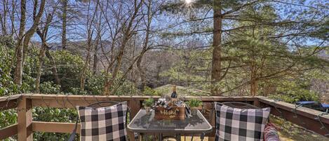 Terraza al aire libre con mesa y sillas, rodeada de árboles y una vista panorámica.