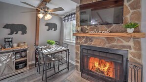 Un salon chaleureux avec une cheminée en pierre, un téléviseur fixé au mur et un ventilateur de plafond.