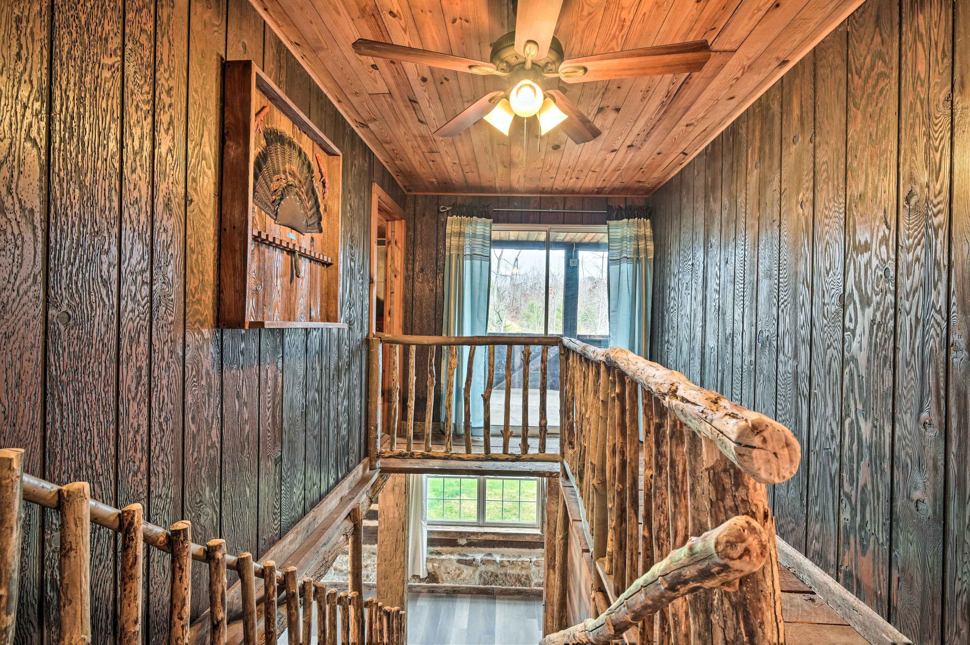 A wooden interior with a ceiling fan, a wooden staircase, and a window with curtains.