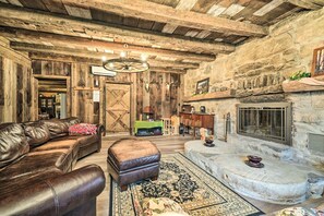 Un interior rústico con sofá de cuero, reposapiés y chimenea de piedra.