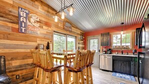 Een rustiek houten interieur met een eettafel en stoelen, een keuken met een spoelbak en kastjes, en een bord met de tekst 'LIVE Bait Tackle Ice & Rentals'.