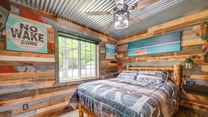 Een knus, landelijk ingerichte kamer met een bed, een bord met daarop 'No Wake Zone', een raam en een plafondventilator.