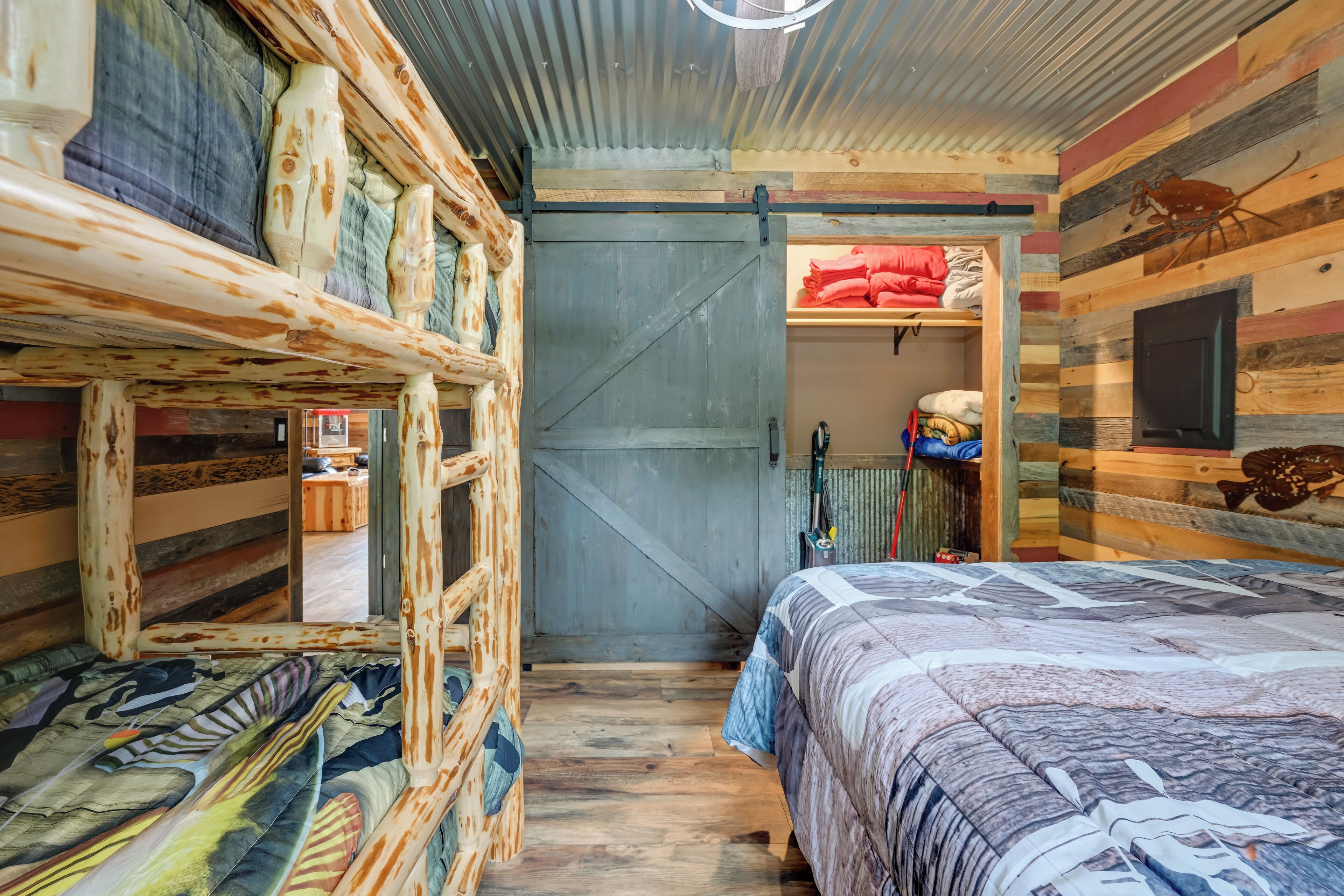 Una habitación rústica tipo cabaña con una cama, una escalera de madera, una puerta y un estante con ropa doblada.