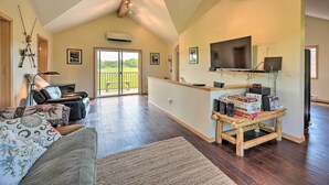 A spacious living room with a high ceiling, a fireplace, a leather sofa, a wooden coffee table, and a television.
