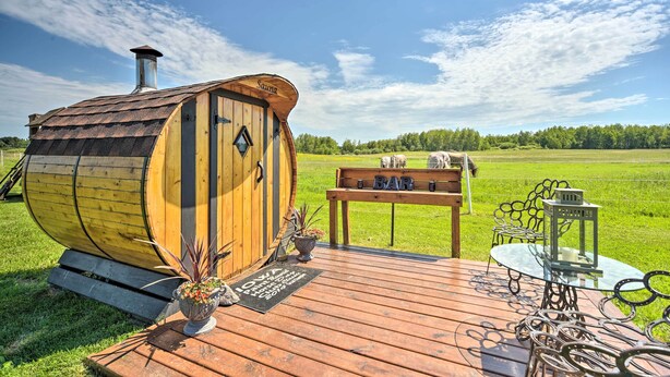 A rustic wooden barrel-shaped structure with a chimney, a wooden deck with a bench and table, and a metal chair.