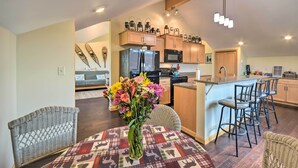 A modern kitchen with a central island, wooden cabinets, and a dining area with wicker chairs and a patterned tablecloth.