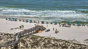 A beach with a wooden boardwalk leading to a lifeguard station, surrounded by beach chairs and umbrellas.