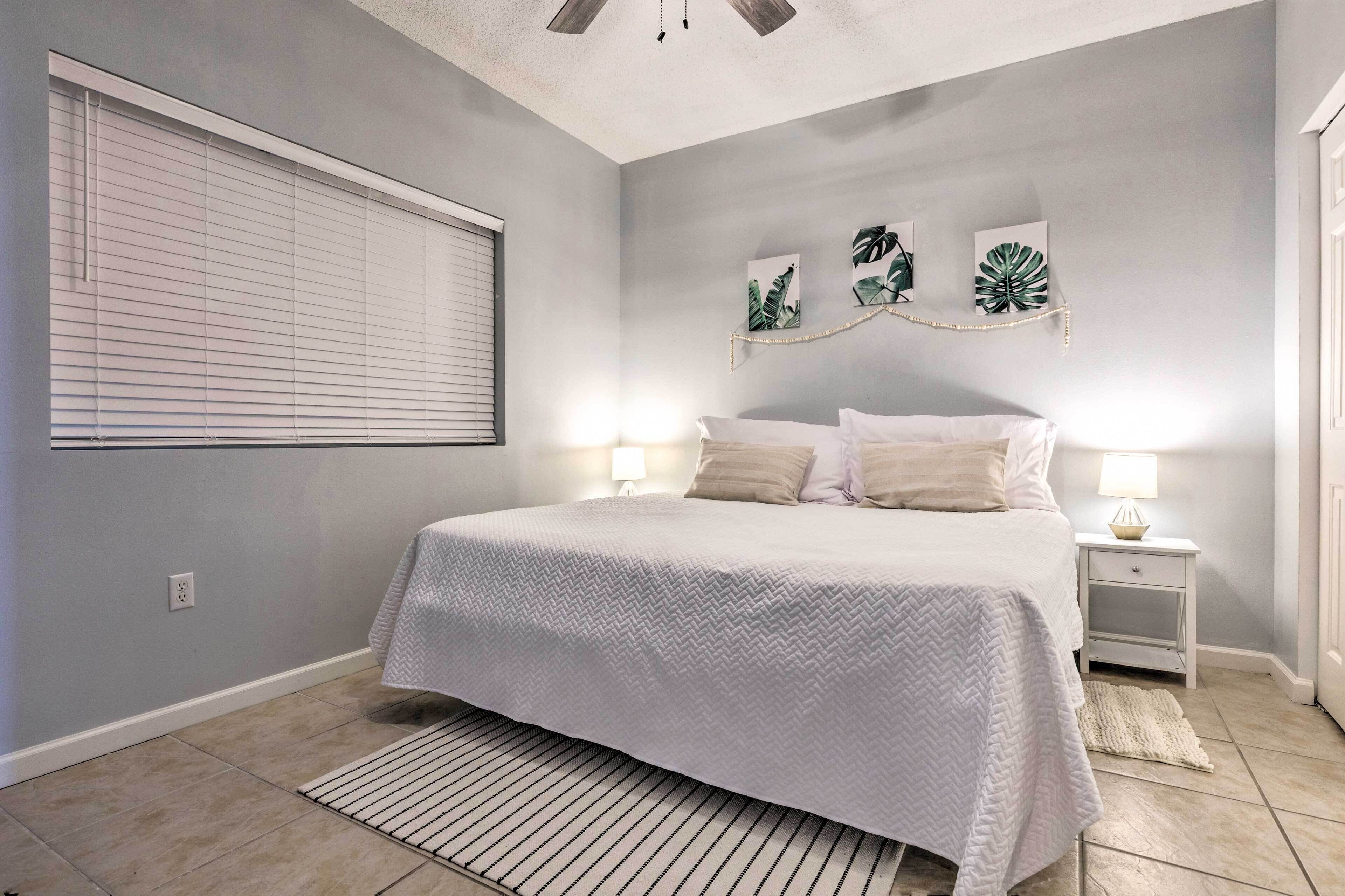 A bedroom with a bed, bedside tables, a window with blinds, and wall art.