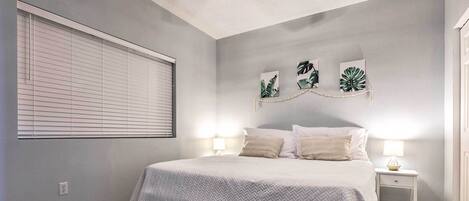 A bedroom with a bed, bedside tables, a window with blinds, and wall art.