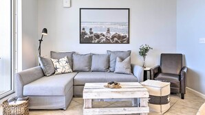 A modern living room with a grey sectional sofa, a white coffee table, a black floor lamp, and a framed picture of a beach scene.