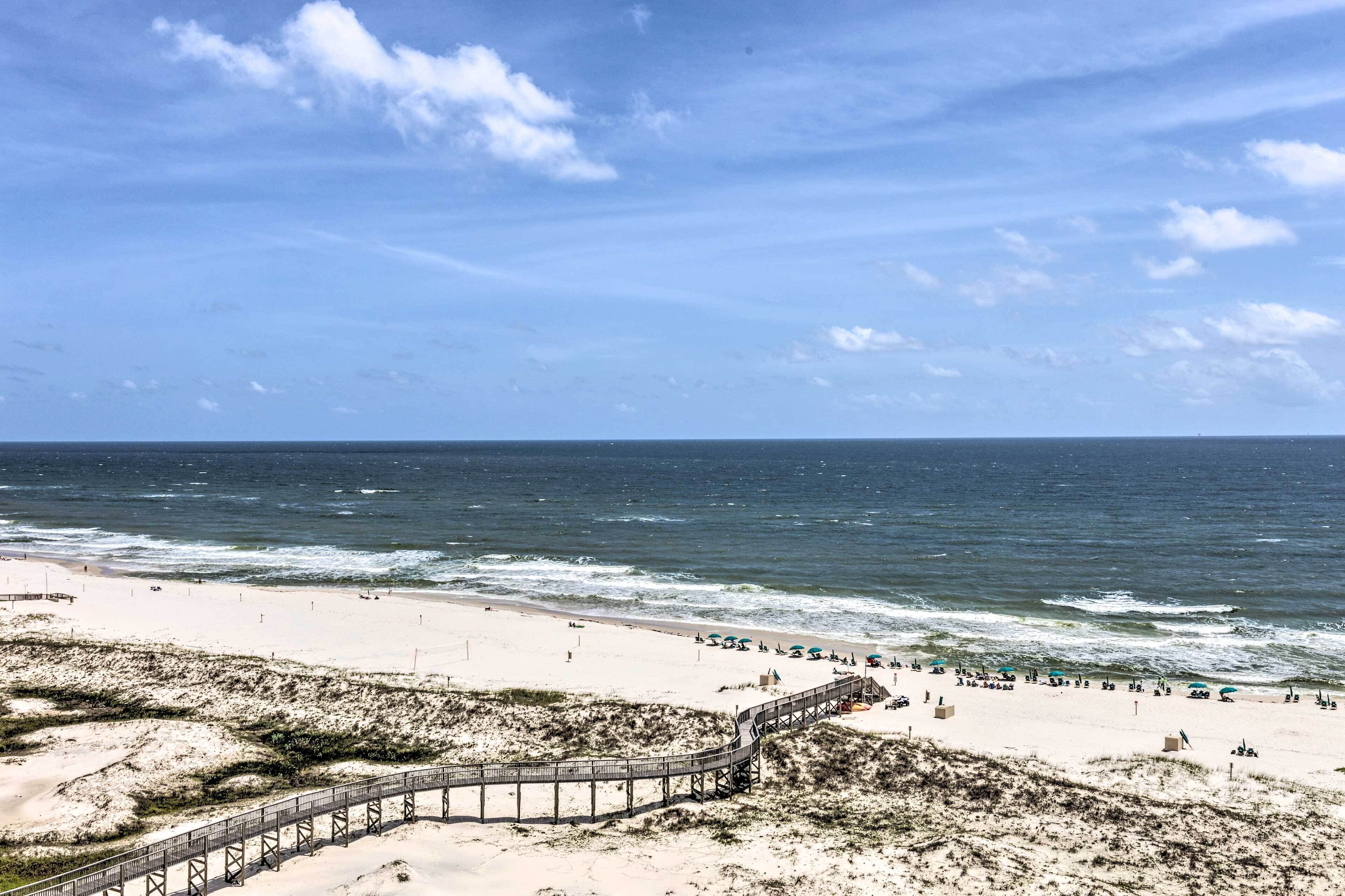 Una playa con un paseo marítimo de madera que conduce a la orilla, arena y océano.