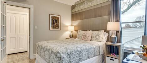 Un dormitorio con cama, mesitas de noche y una ventana con cortinas.