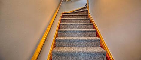 A carpeted staircase with wooden handrails and a white wall.