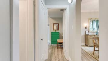 Un pasillo con suelo de madera, un aparador verde y una silla.